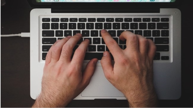A man's hands typing on his laptop.